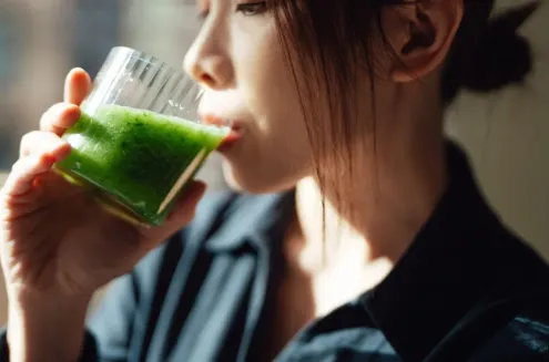 Person drinking green smoothie in sunlight